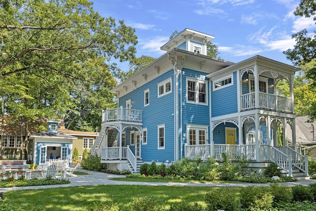 italianate-style house with an outbuilding, a balcony, and a front yard