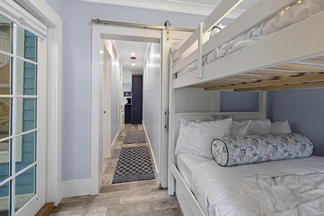 bedroom with a barn door, wood finished floors, and baseboards