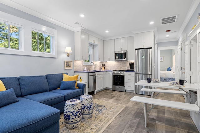 living room featuring recessed lighting, light wood-style floors, visible vents, and ornamental molding