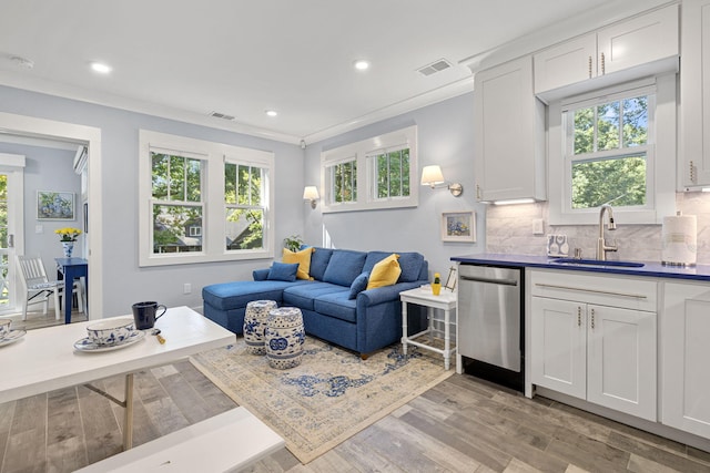 living area with crown molding, a healthy amount of sunlight, visible vents, and light wood finished floors