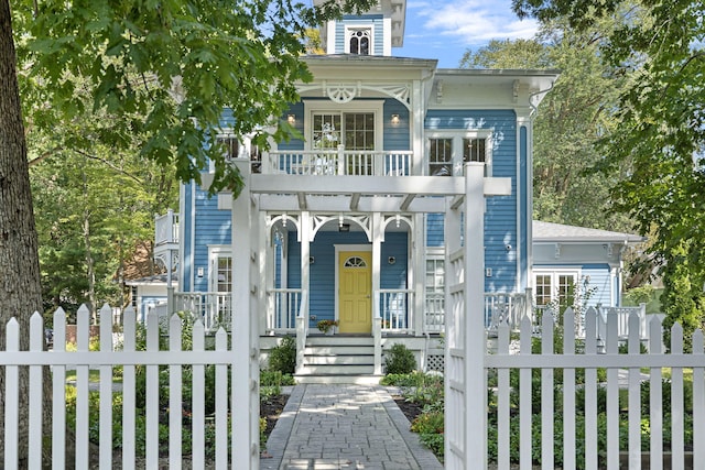 italianate home featuring a fenced front yard, a balcony, and covered porch
