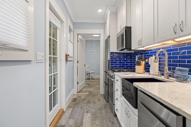 kitchen with backsplash, ornamental molding, light wood-style flooring, appliances with stainless steel finishes, and white cabinets