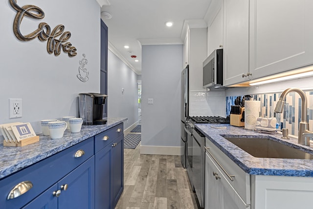 kitchen featuring light wood finished floors, stainless steel microwave, tasteful backsplash, blue cabinets, and a sink