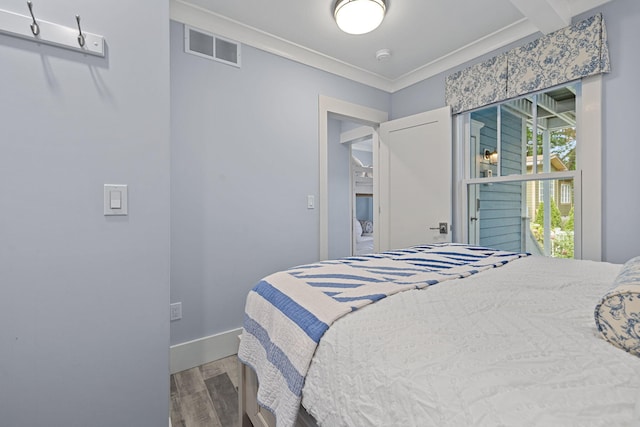 bedroom with ornamental molding, wood finished floors, visible vents, and baseboards