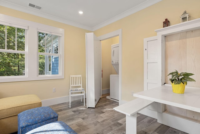 living area featuring visible vents, ornamental molding, wood finished floors, stacked washing maching and dryer, and baseboards