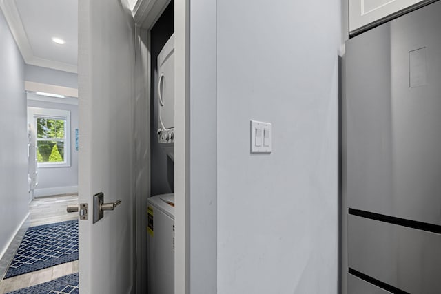 clothes washing area featuring recessed lighting, crown molding, stacked washer / drying machine, baseboards, and laundry area