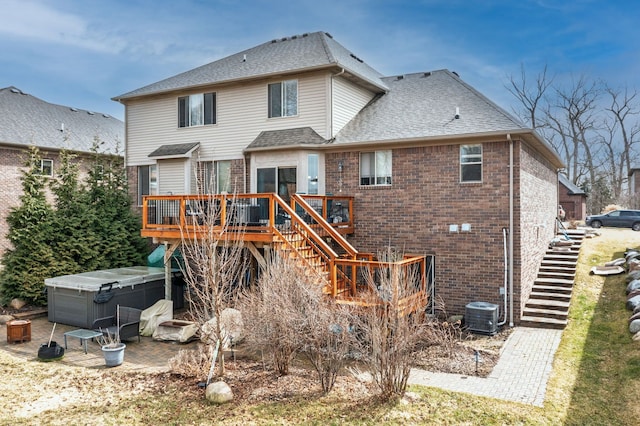 rear view of house with stairway, a hot tub, a wooden deck, brick siding, and roof with shingles