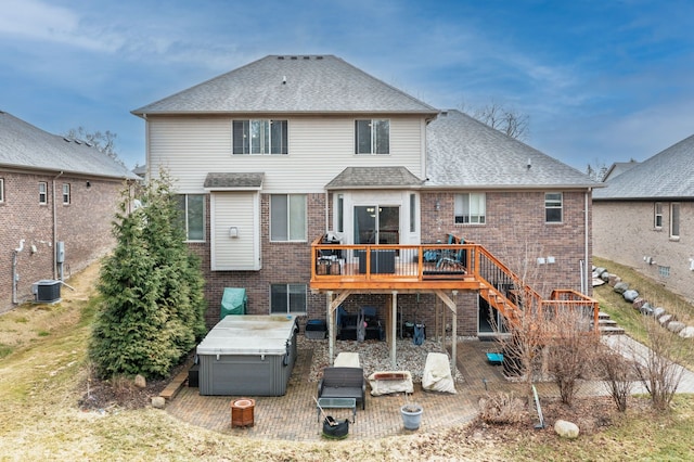 rear view of property featuring roof with shingles, brick siding, a hot tub, stairs, and a deck