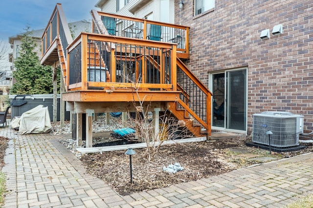 back of property with cooling unit, brick siding, a wooden deck, and stairway