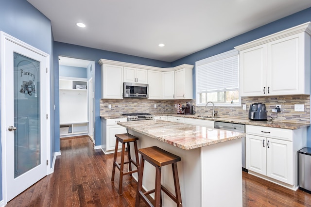 kitchen featuring white cabinets, a kitchen breakfast bar, stainless steel appliances, a sink, and a center island