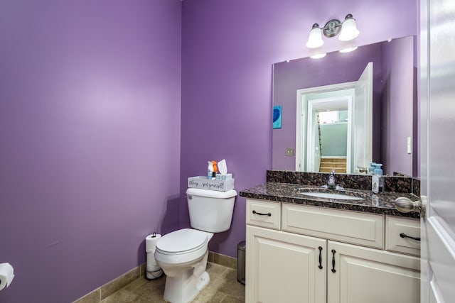 half bath with baseboards, tile patterned flooring, vanity, and toilet