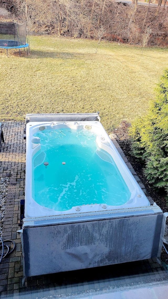 view of pool featuring a lawn, a hot tub, and a trampoline