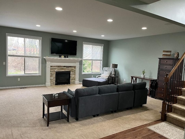 carpeted living room with recessed lighting, stairway, a stone fireplace, wood finished floors, and baseboards