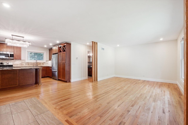 kitchen featuring backsplash, open floor plan, appliances with stainless steel finishes, brown cabinetry, and light countertops