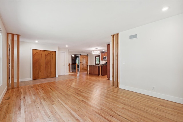 unfurnished living room with visible vents, baseboards, a barn door, recessed lighting, and light wood-style floors