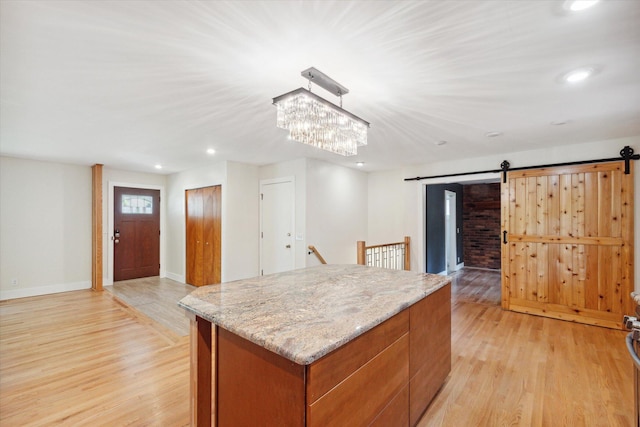 kitchen with a center island, light stone countertops, a barn door, recessed lighting, and light wood-style floors