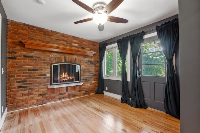 unfurnished room featuring ceiling fan, wood finished floors, brick wall, and a fireplace