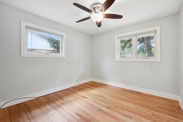 spare room with a ceiling fan, visible vents, wood finished floors, and baseboards