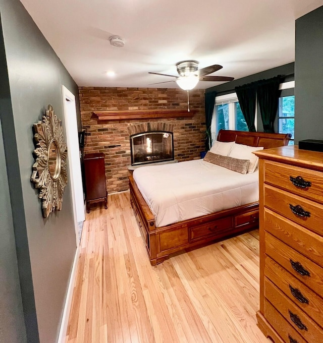 bedroom featuring light wood-style flooring, baseboards, brick wall, and ceiling fan