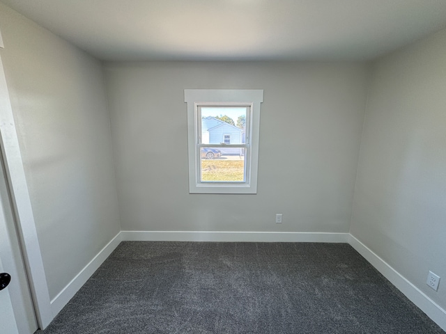 spare room featuring baseboards and dark colored carpet