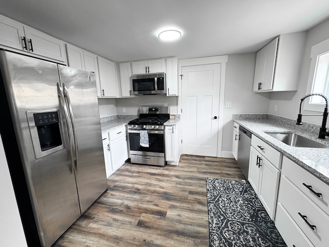 kitchen with light stone counters, stainless steel appliances, wood finished floors, a sink, and white cabinetry