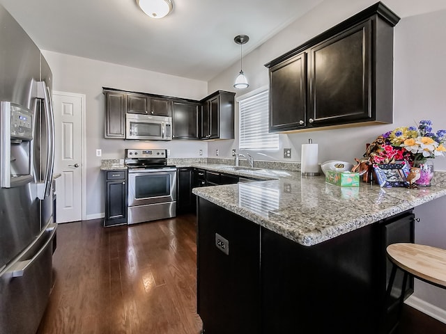 kitchen featuring a sink, light stone counters, a peninsula, stainless steel appliances, and dark wood-style flooring