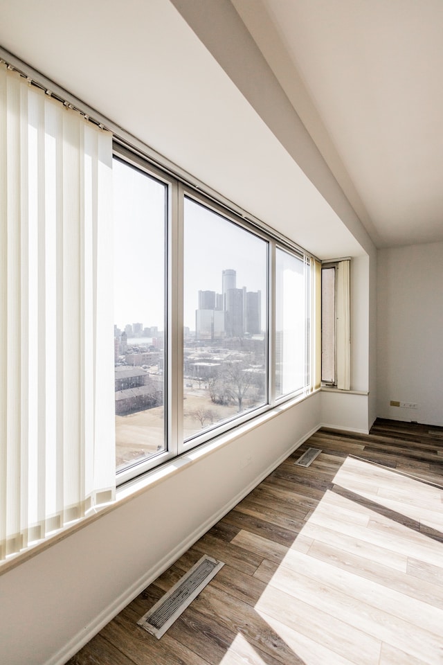 unfurnished room featuring visible vents, a city view, and wood finished floors