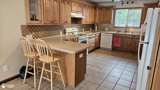 kitchen with white appliances, under cabinet range hood, a sink, a peninsula, and a kitchen breakfast bar