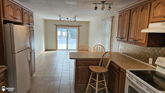 kitchen with white appliances, under cabinet range hood, backsplash, a peninsula, and a breakfast bar