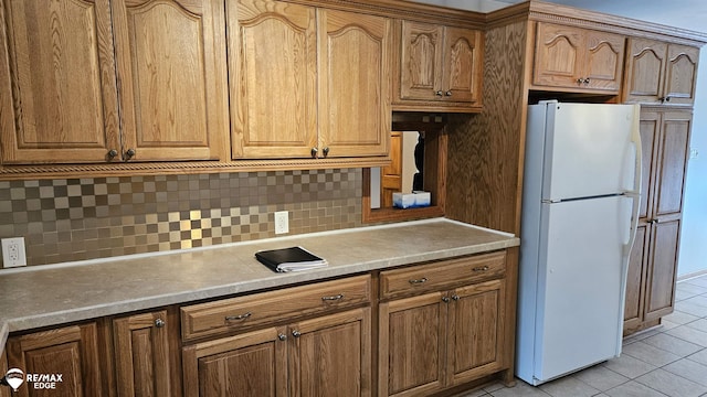 kitchen with freestanding refrigerator, light tile patterned floors, backsplash, and brown cabinetry