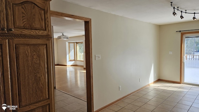 empty room featuring rail lighting, light tile patterned floors, and baseboards