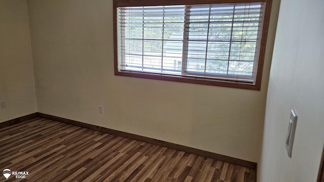 empty room featuring plenty of natural light, dark wood finished floors, and baseboards