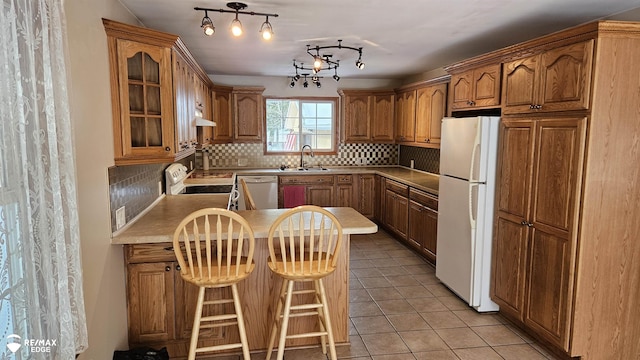 kitchen featuring white appliances, a sink, a peninsula, glass insert cabinets, and brown cabinets