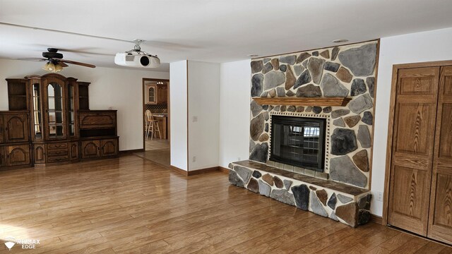 living room with light wood-style floors, a ceiling fan, a stone fireplace, and baseboards