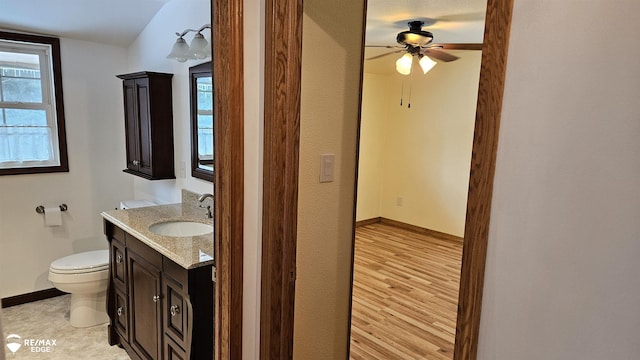 bathroom featuring toilet, vanity, baseboards, ceiling fan, and healthy amount of natural light