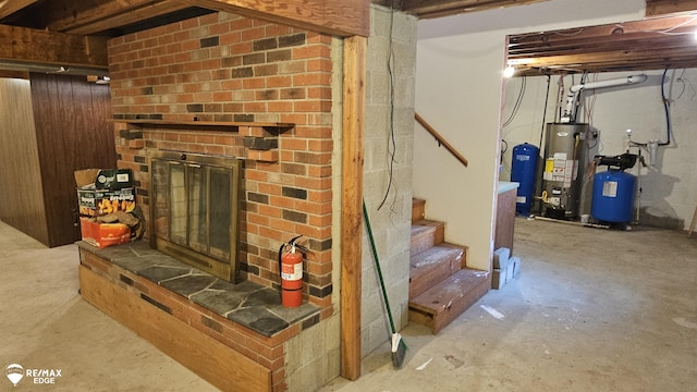 finished basement featuring water heater, a brick fireplace, stairway, and a water pressure tank