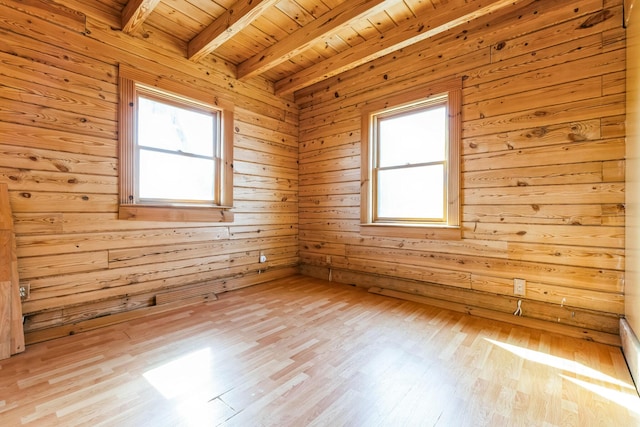 empty room with beamed ceiling, plenty of natural light, and light wood-style flooring