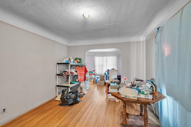 interior space with arched walkways, a textured ceiling, baseboards, and hardwood / wood-style flooring