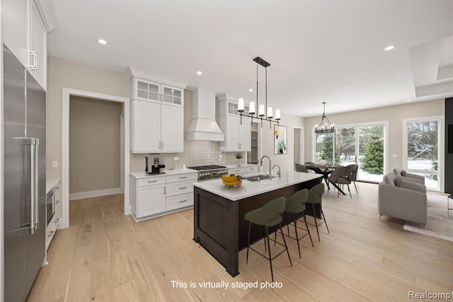 kitchen with premium range hood, a notable chandelier, premium appliances, light wood-style floors, and decorative backsplash