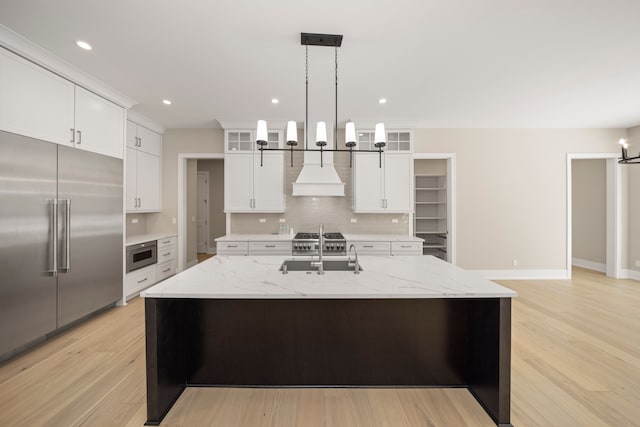 kitchen with light wood finished floors, a sink, decorative backsplash, glass insert cabinets, and built in refrigerator