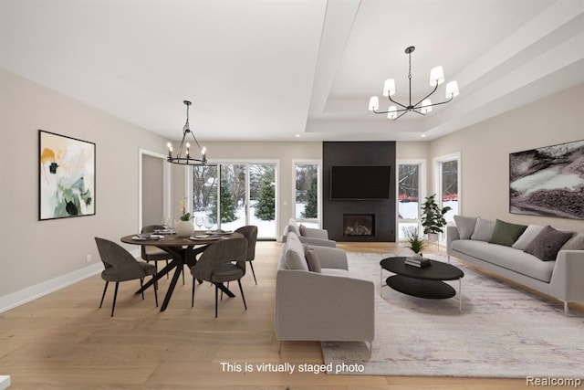 living area with a notable chandelier, light wood-type flooring, a raised ceiling, and baseboards