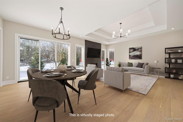 dining room with a tray ceiling, baseboards, a notable chandelier, and light wood finished floors