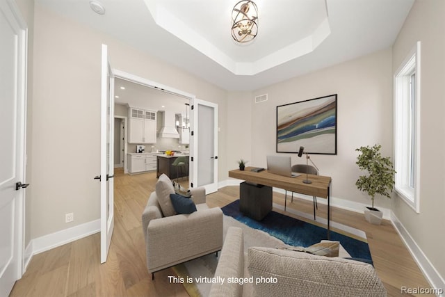 office space with a tray ceiling, french doors, visible vents, and light wood-type flooring