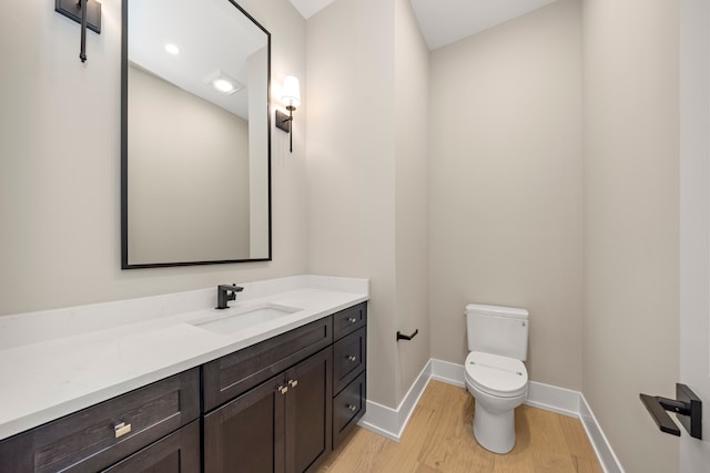 half bath featuring vanity, toilet, wood finished floors, and baseboards