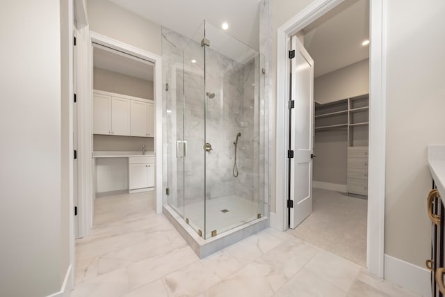 full bath with a marble finish shower, marble finish floor, a walk in closet, and baseboards