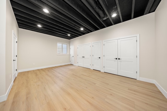 unfurnished bedroom with beam ceiling, baseboards, multiple closets, and light wood-type flooring