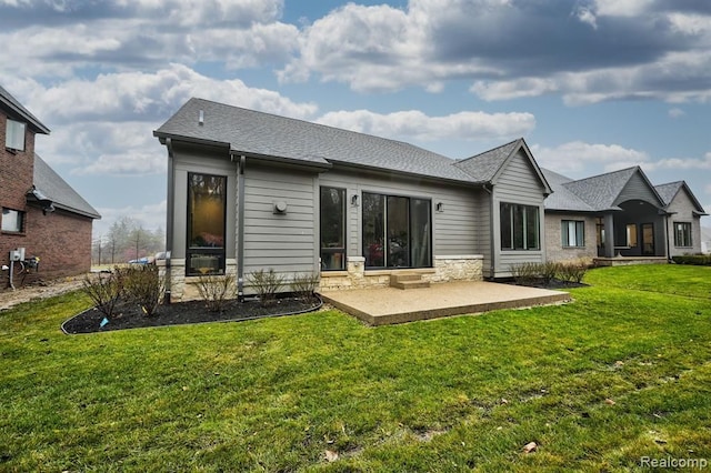 back of house featuring a patio, a lawn, stone siding, and a shingled roof