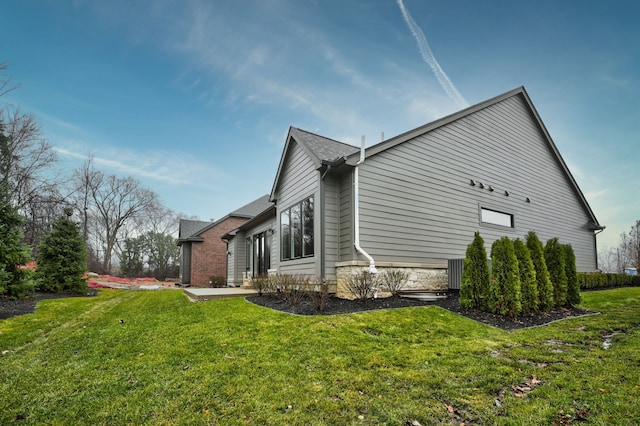 view of property exterior with central air condition unit, a shingled roof, and a yard