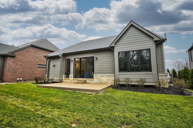 rear view of house featuring a yard, stone siding, a shingled roof, and a patio area