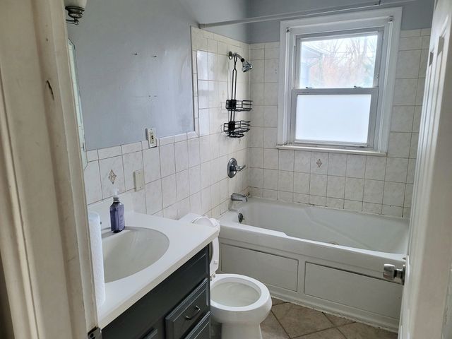 full bath featuring vanity, tile patterned flooring, shower / bath combination, tile walls, and toilet